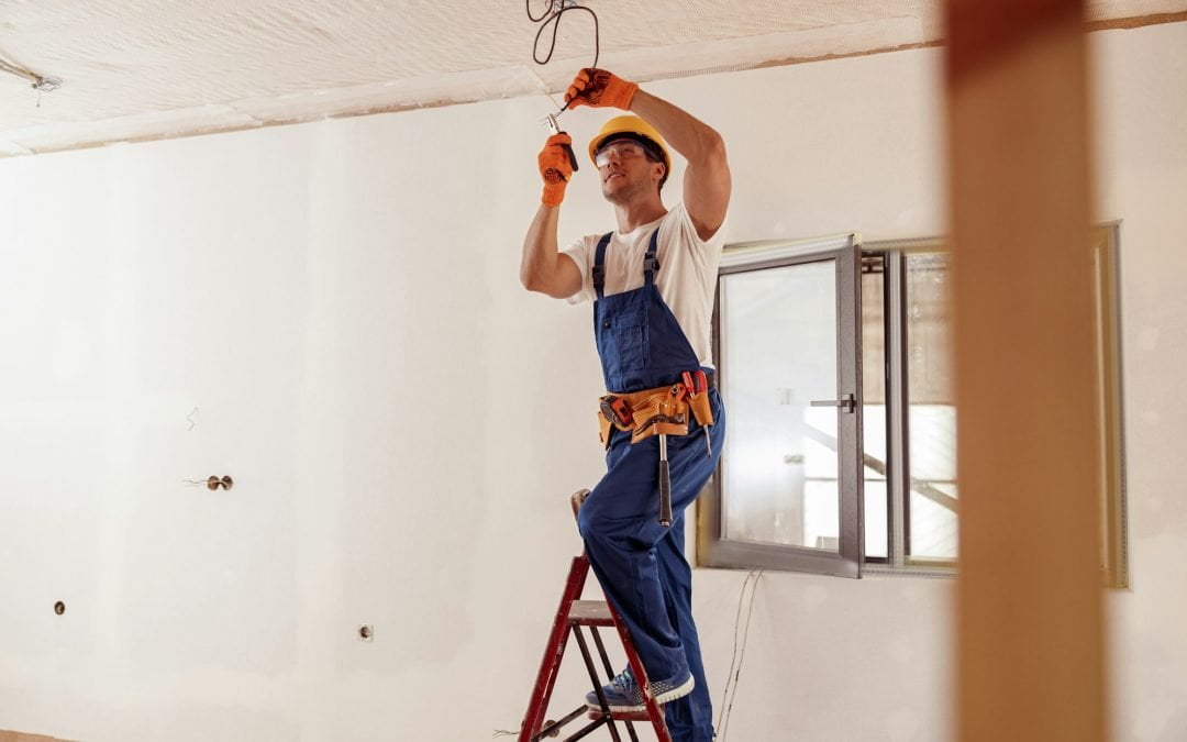 Smiling electrician fixing electric cable on ceiling